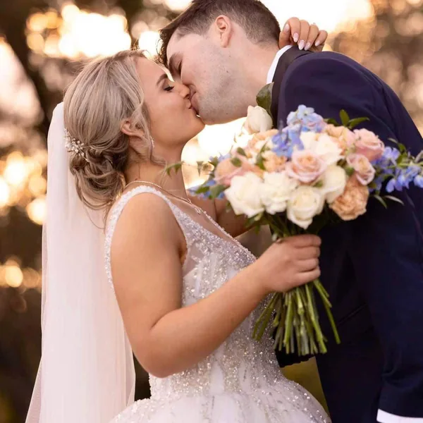 A bride and groom kiss, her bouquet in hand