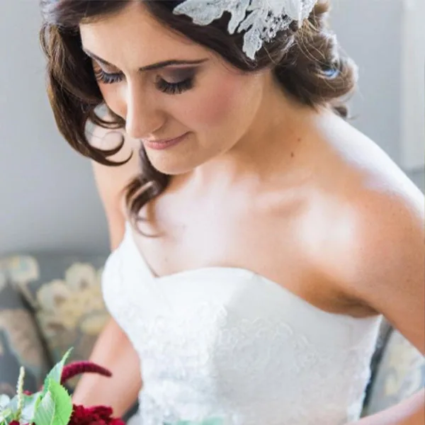 A bride with a lace headpiece looking down at her bouquet