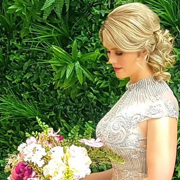 A bride with a soft blonde updo holding a colourful bouquet