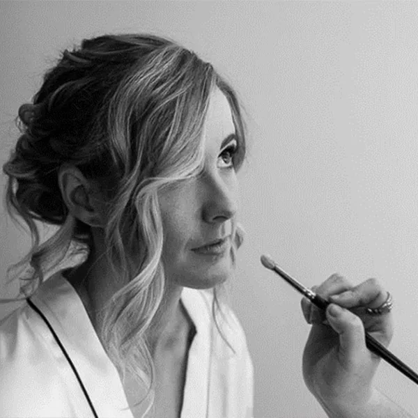 A black and white photo of a bride having her makeup applied